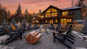 A lodge with a fire pit and outdoor seating, surrounded by trees and a clear sky.