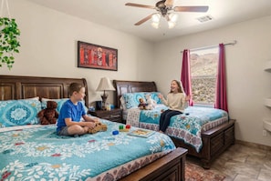 A bedroom with two beds, a ceiling fan, a window with curtains, and a wall-mounted picture. - Private Estate Pool Views Events Welcome (Las Cruces)