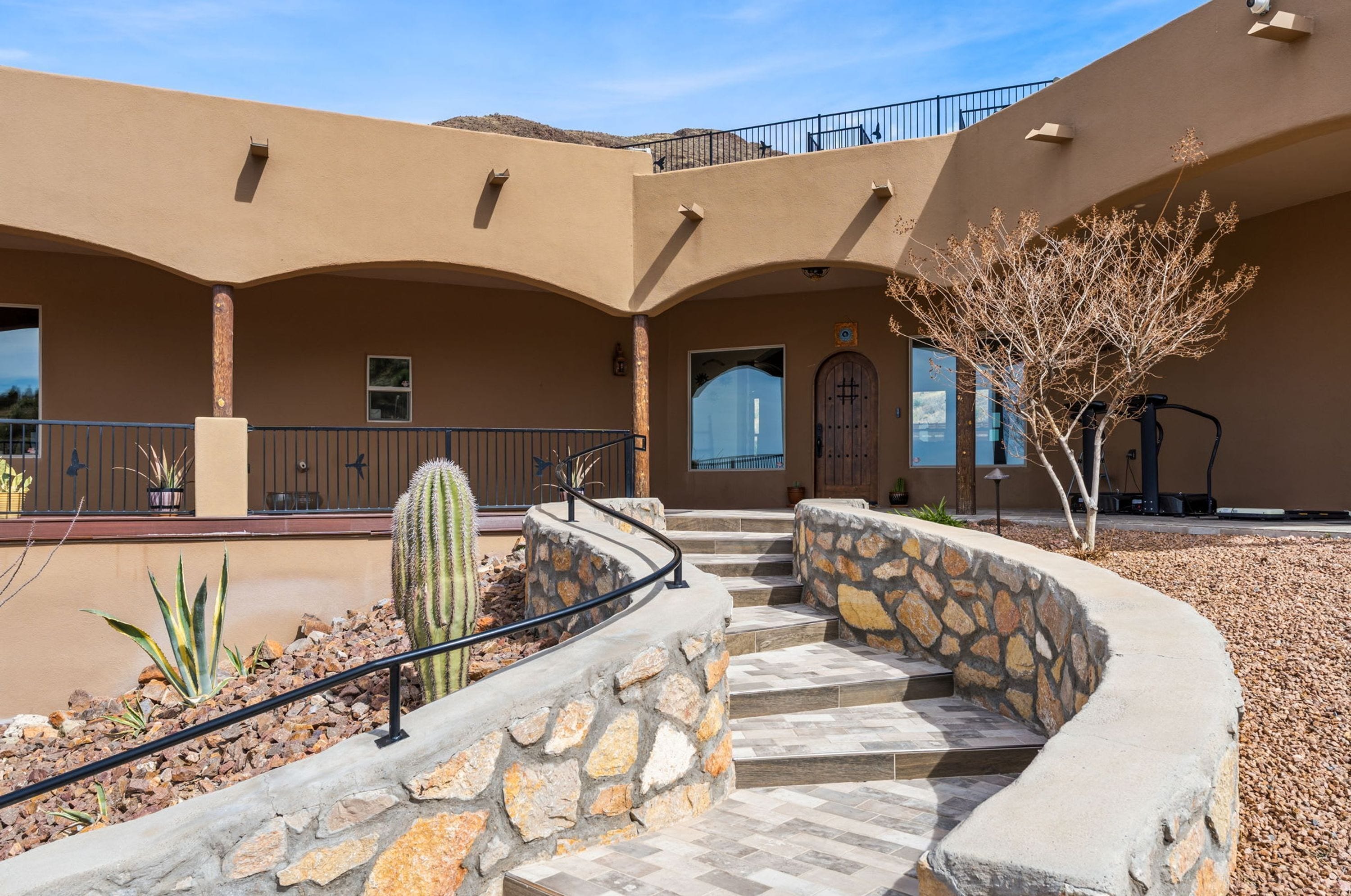 A building with a curved stone staircase, a cactus, and a tree in the courtyard.