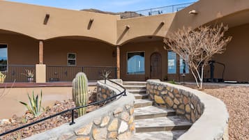 A building with a curved stone staircase, a cactus, and a tree in the courtyard.