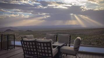 An outdoor deck with a table and chairs, overlooking a desert landscape with mountains in the distance.