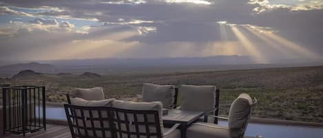 Una terraza al aire libre con una mesa y sillas, con vistas a un paisaje desértico y montañas a lo lejos.