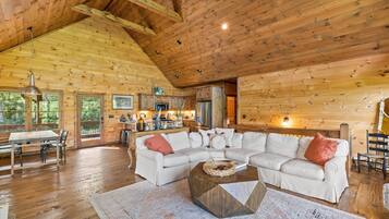 A spacious living room with a large L-shaped sectional sofa, a coffee table, and a dining area with a wooden table and chairs.