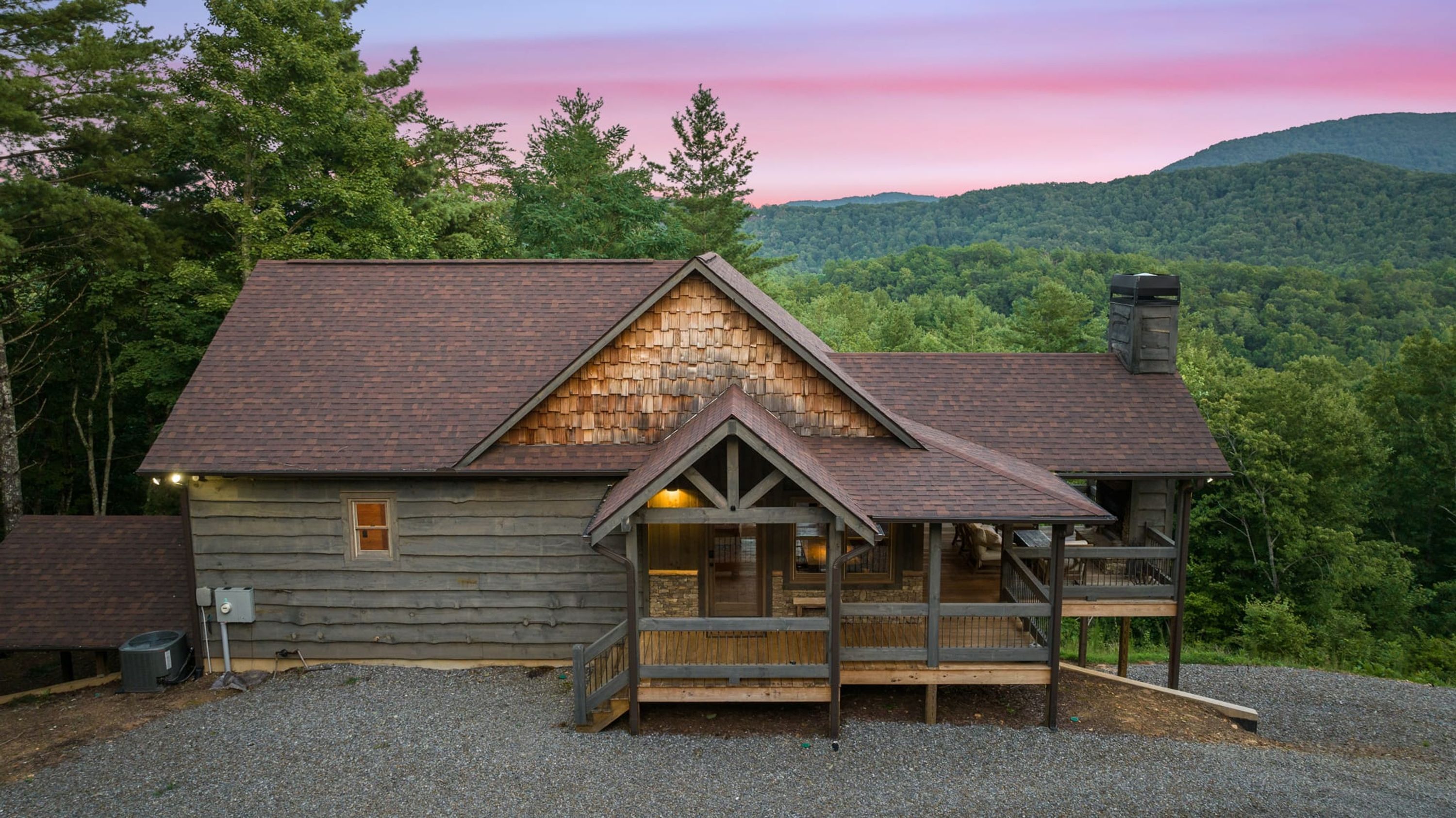 A rustic cabin with a stone gable roof, wooden porch, and a gravel driveway.