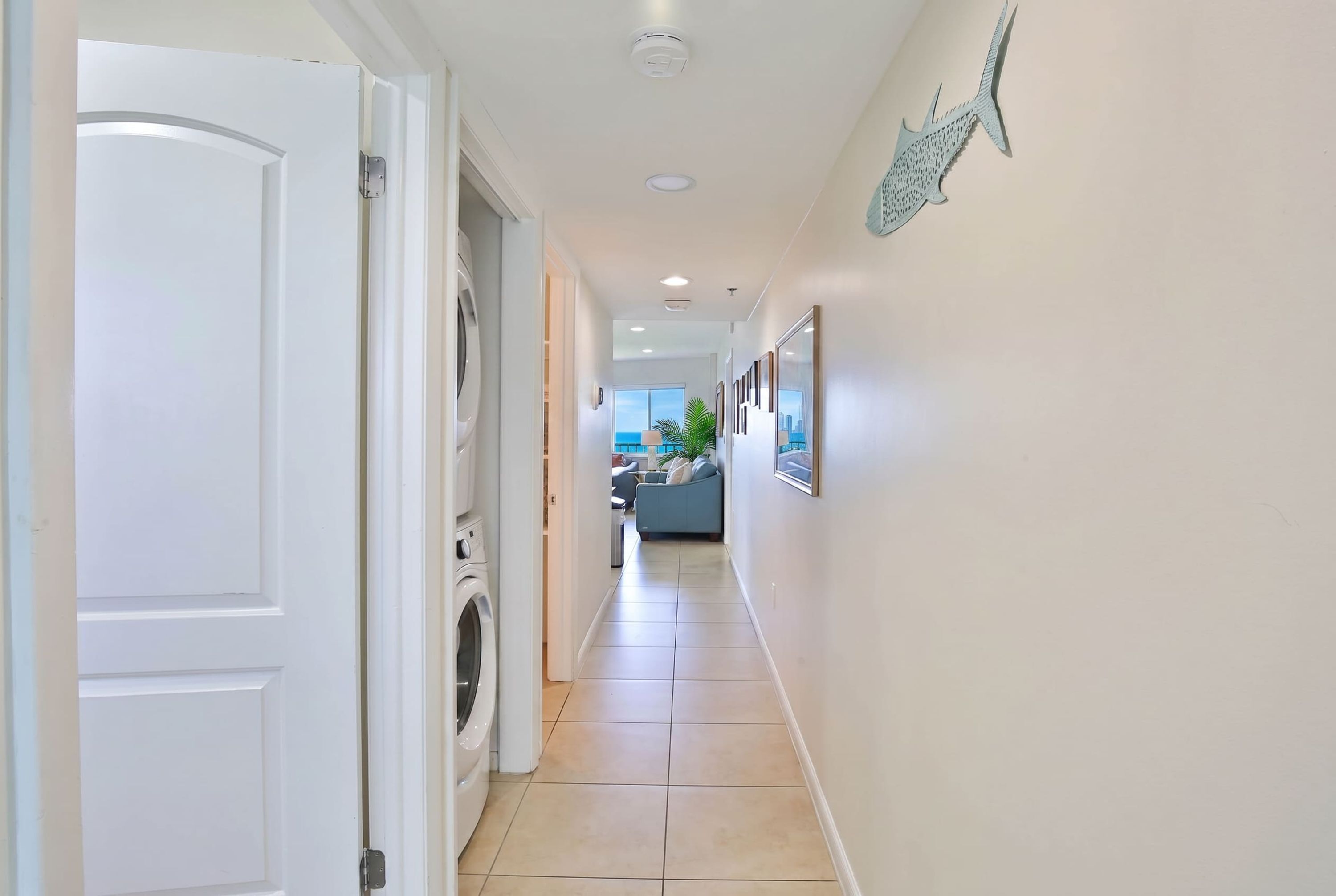 A hallway with a washing machine, a door, and a view of a living area with a sofa and a plant.