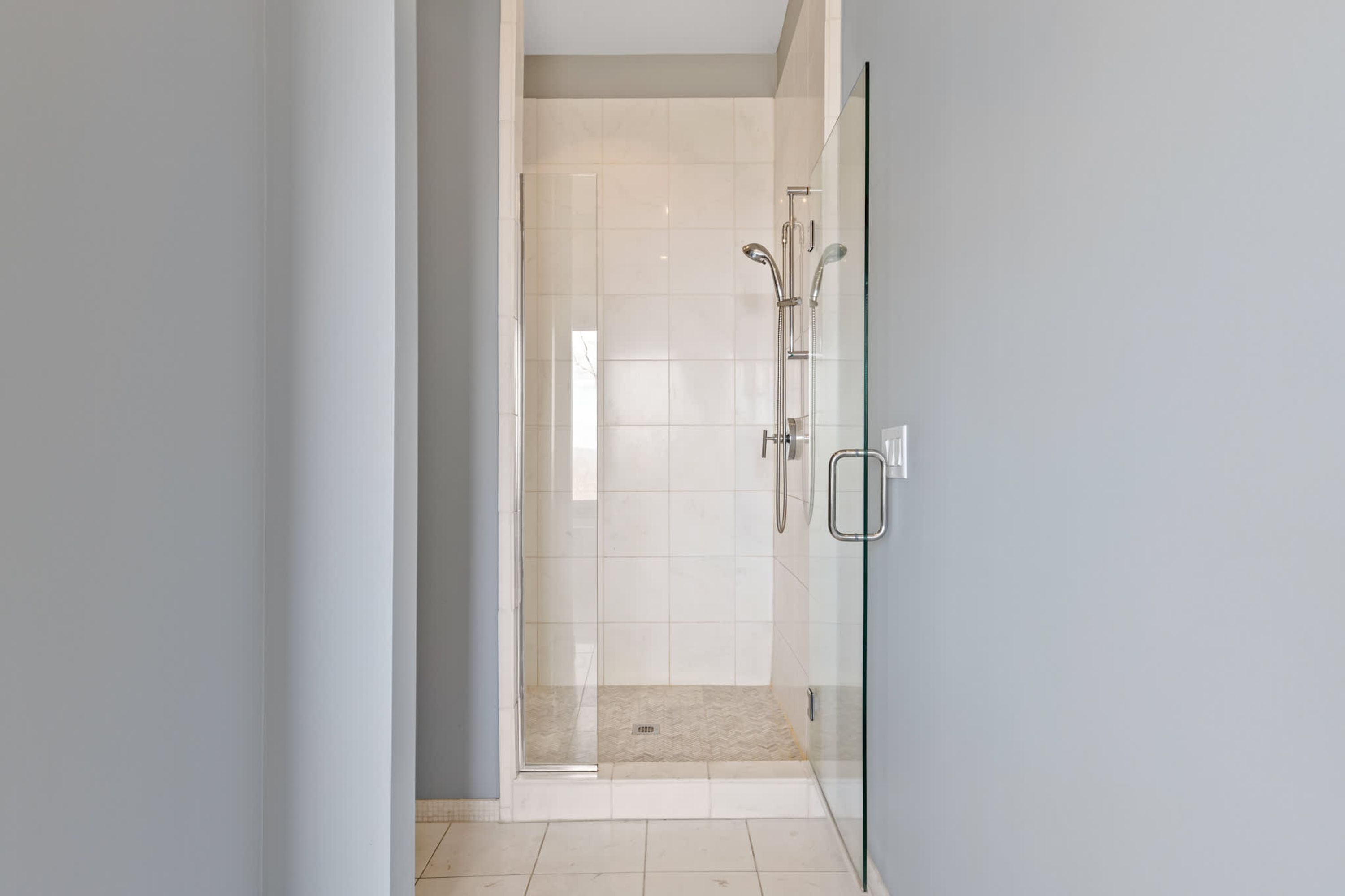 Un baño moderno con cabina de ducha de vidrio, ducha expuesta y suelo de baldosas.