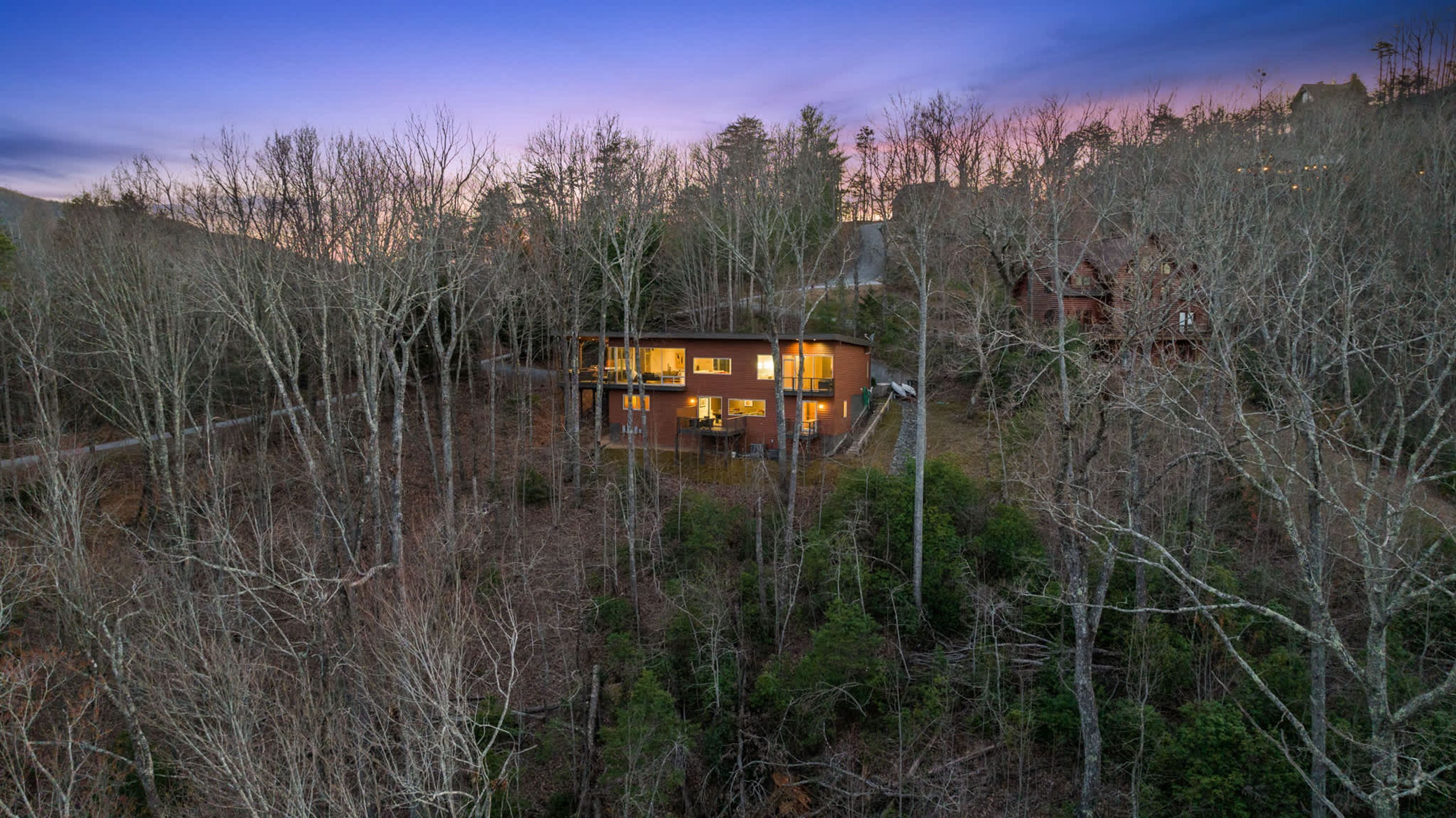 Une maison à deux étages entourée d’arbres, dotée d’un balcon bien visible et offrant une vue dégagée sur la forêt environnante.