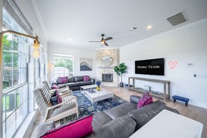 A modern living room with a fireplace, a television, and a large window. - Austin Luxe Retreat Pool Spa Game Room Fire Pit (Austin)