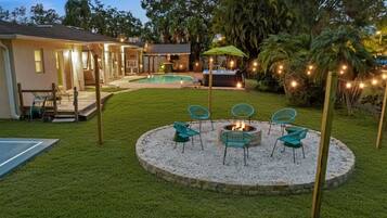 Un patio trasero con un brasero, mobiliario exterior, una piscina y un porche cubierto.