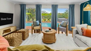 Ein modernes Wohnzimmer mit Blick auf einen Pool, einem Flachbildfernseher und einer gemütlichen Sitzecke.