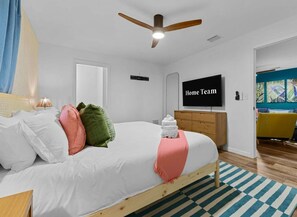 Ein modernes Schlafzimmer mit einem Bett, Kissen, einem Fernseher, einer Holzkommode und einem Streifen Teppich.