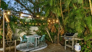 Eine Terrasse im Freien mit einem runden Tisch und Stühlen, einem Grill und Lichterketten.