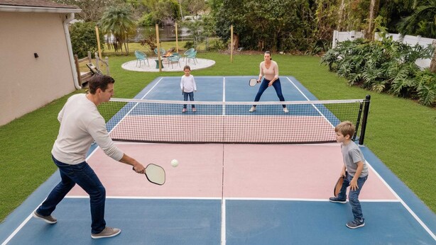 Ein Tennisplatz im Freien mit Netz, umgeben von Grünflächen und einer kleinen Sitzecke.