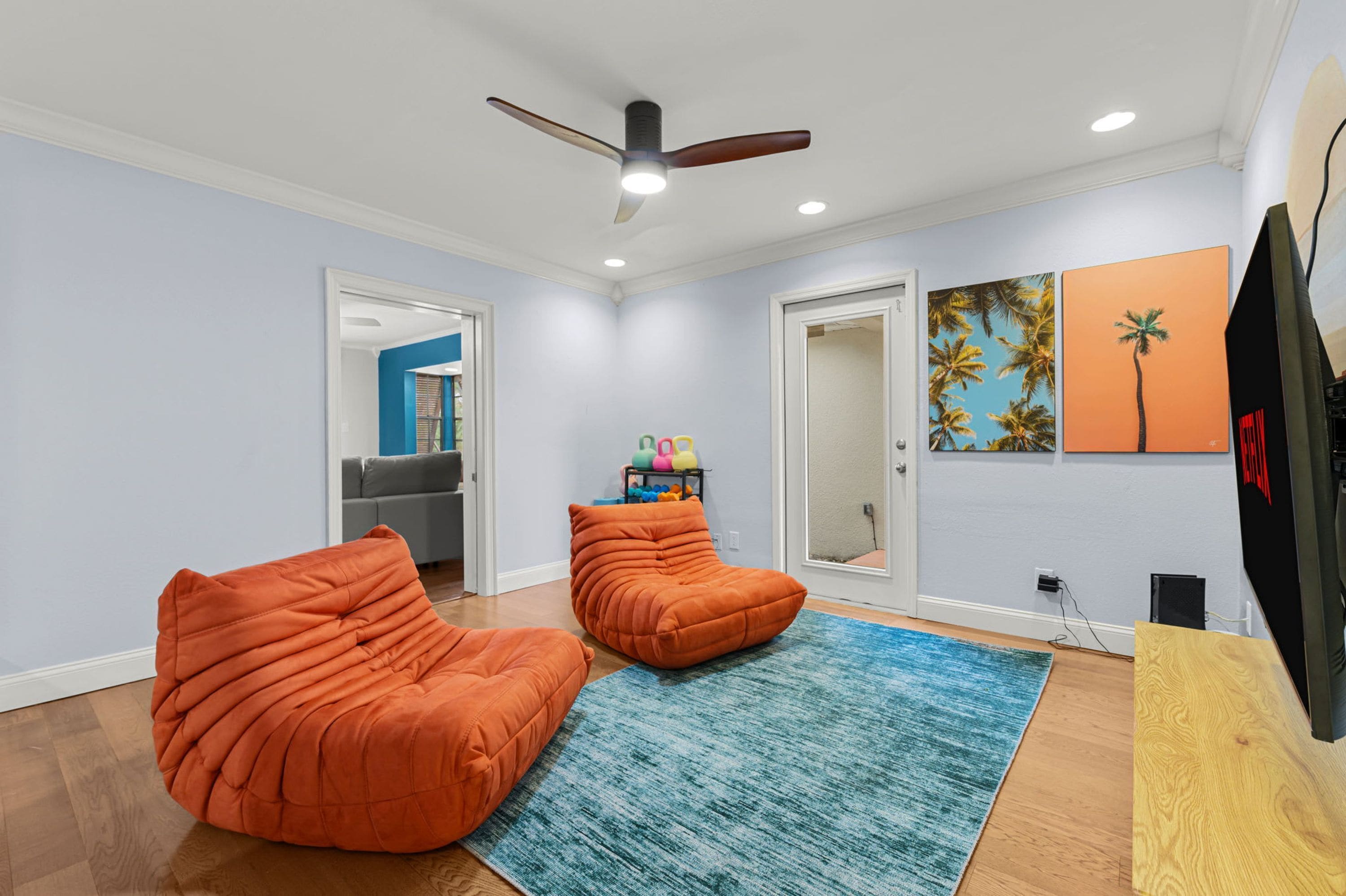 Una habitación con dos sillones de mimbre naranja, un ventilador de techo y una alfombra azul.