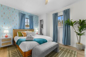 Un dormitorio con cama, mesitas de noche, lámpara, planta y cortinas.