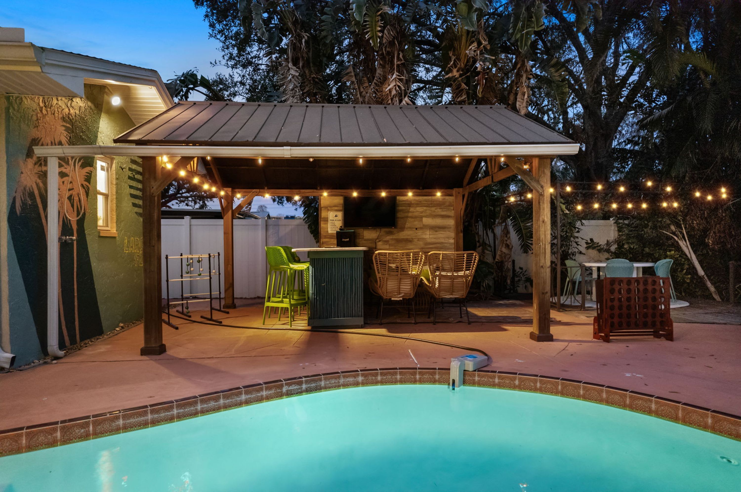 Un espacio al aire libre techado con piscina, asientos y luces colgantes.