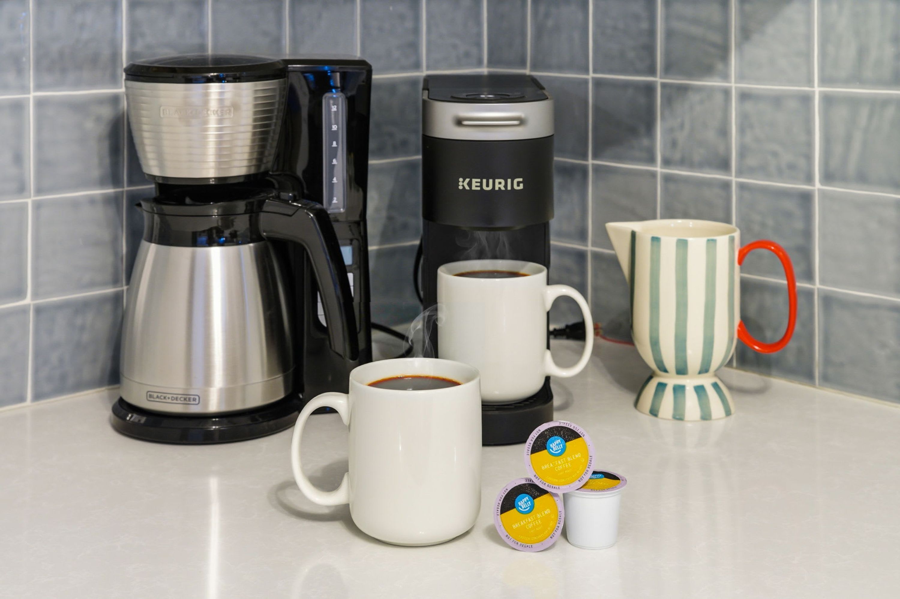 Eine Kaffeemaschine, zwei Tassen und eine Kanne auf einer Arbeitsplatte mit Fliesen.