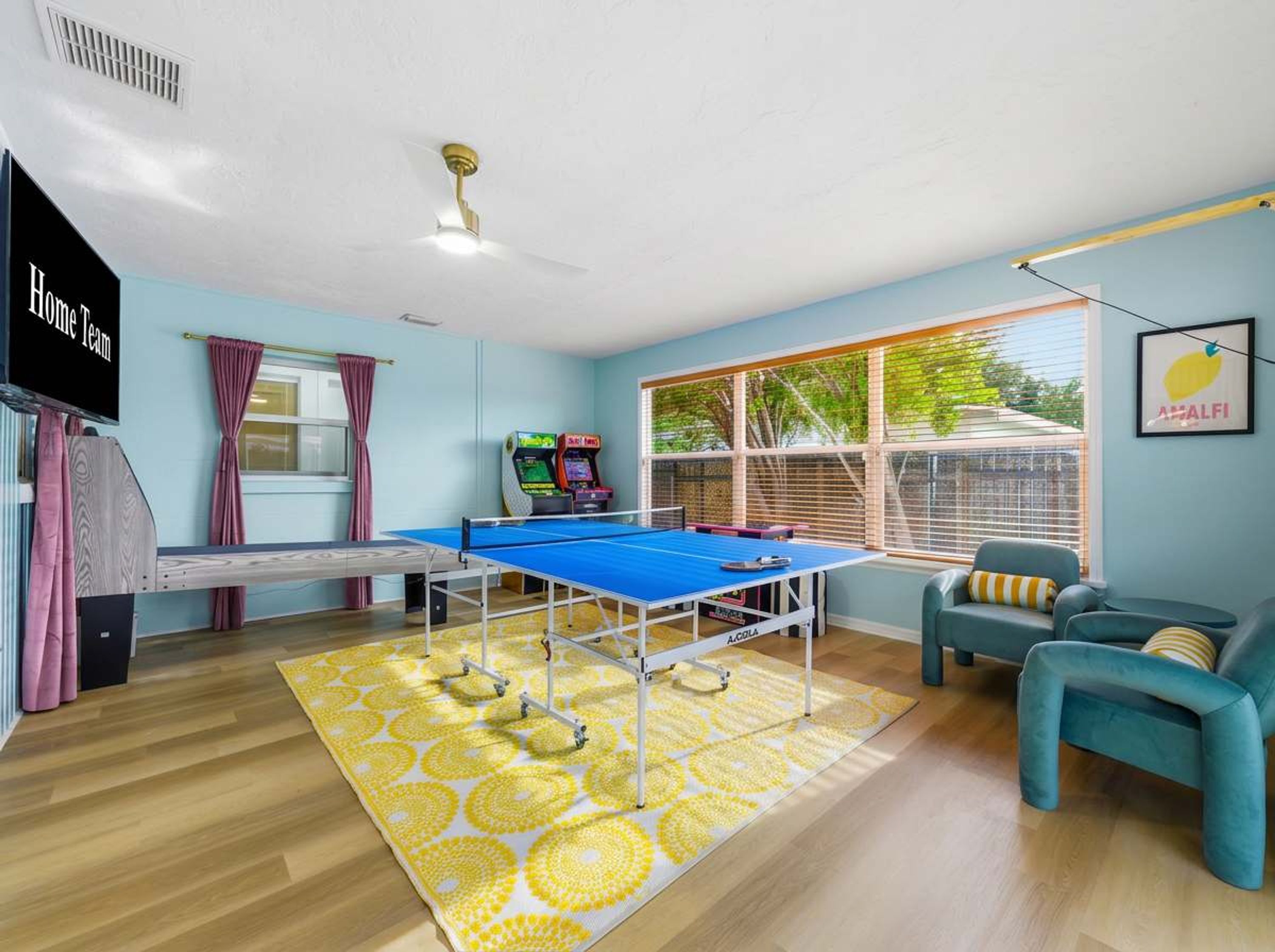 Una habitación con mesa de ping pong, sofá, ventana con persianas y ventilador de techo.