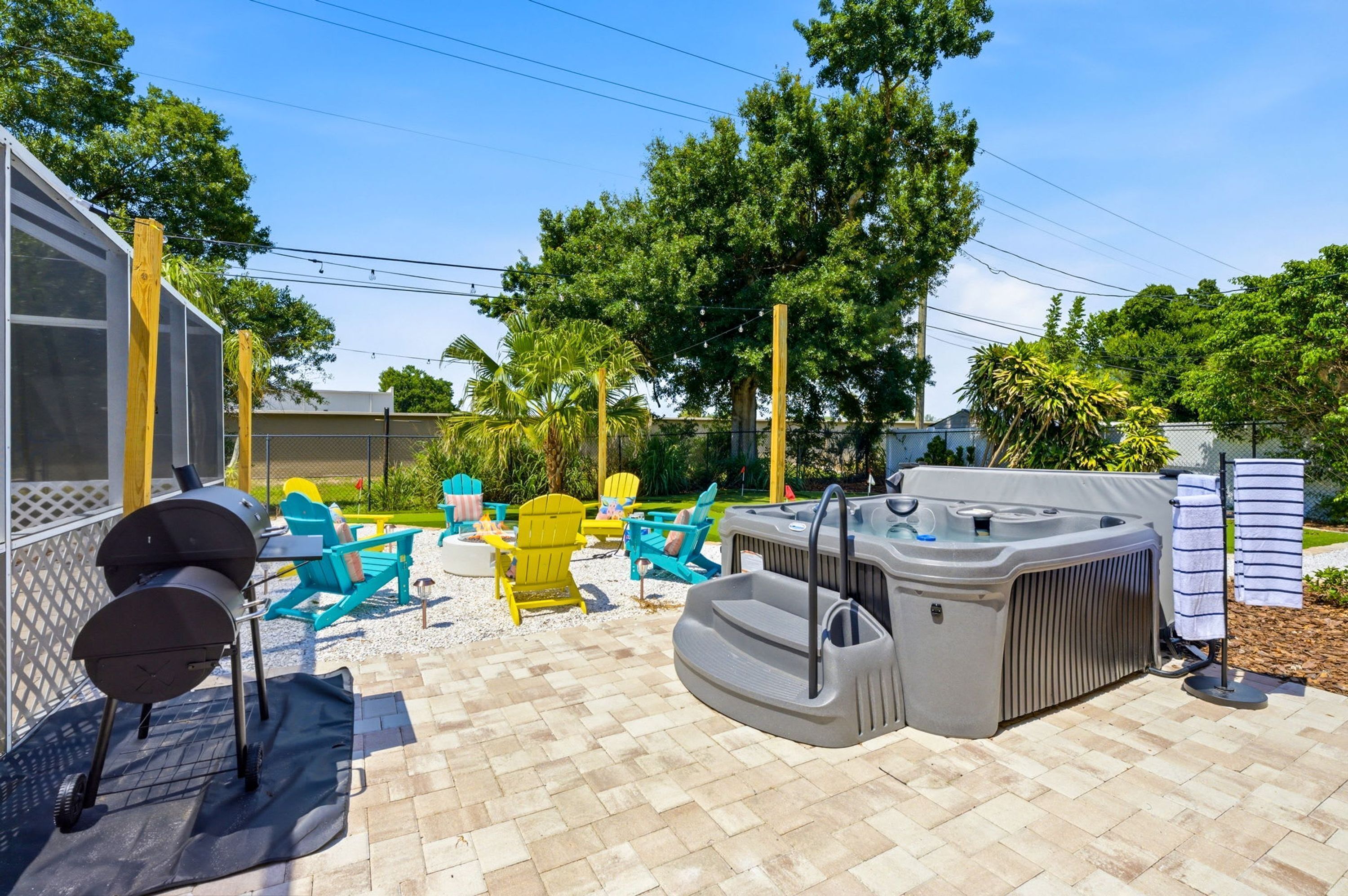 An outdoor patio area with a hot tub, Adirondack chairs, and a grill.