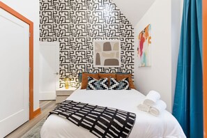 A hotel room with a patterned wall, a bed with white linens, a black and white throw blanket, and a blue curtain. - Victory Lane Villa Game Room - Hot Tub - Firepit (Indianapolis)