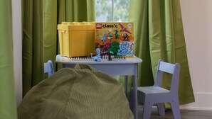 A room with a window, green curtains, a yellow LEGO box, a white table, a blue chair, and a bean bag. - Victory Lane Villa Game Room - Hot Tub - Firepit (Indianapolis)