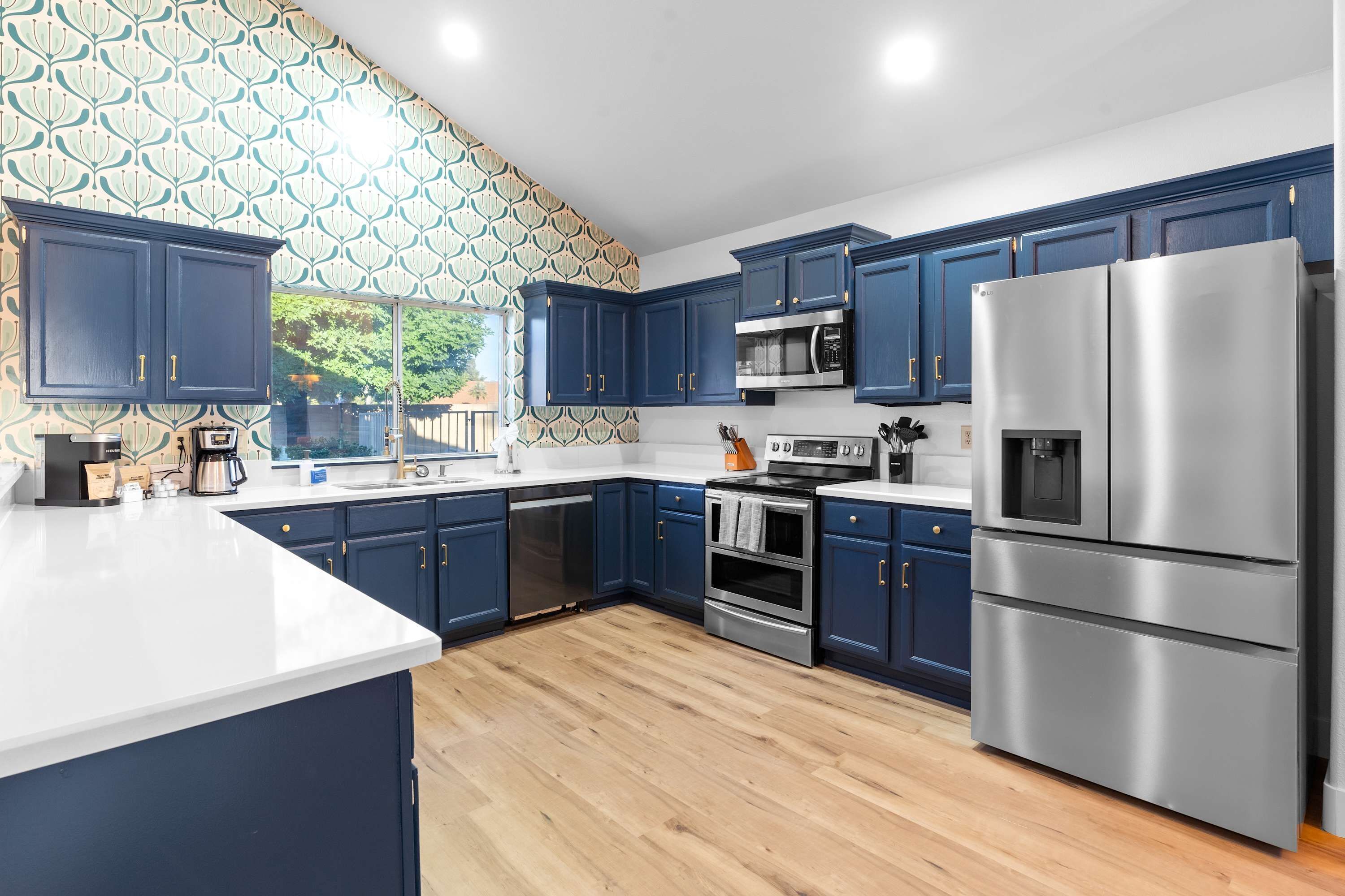 A modern kitchen with dark blue cabinets, stainless steel appliances, and a patterned wallpaper.