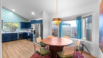 A modern kitchen with blue cabinets, a stainless steel refrigerator, and a dining area with a round table and chairs.