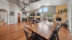 A spacious kitchen with modern appliances, a dining area with a large wooden table, and a stone fireplace. - The Juniper Pickleball Private Pool (Fredericksburg)