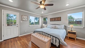 A bedroom with a bed, a bench, a ceiling fan, and two windows. - The Juniper Pickleball Private Pool (Fredericksburg)