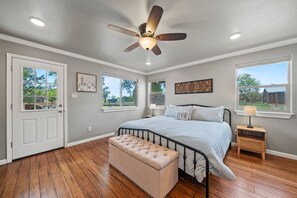Ein Schlafzimmer mit einem Bett, einer Bank, einem Deckenventilator und zwei Fenstern.