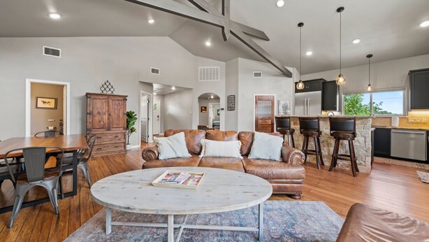 A spacious living area with a dining table, leather sofa, and a kitchen area with bar stools. - The Juniper Pickleball Private Pool (Fredericksburg)