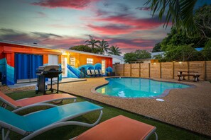 Un jardin avec une piscine, des chaises longues et un barbecue.