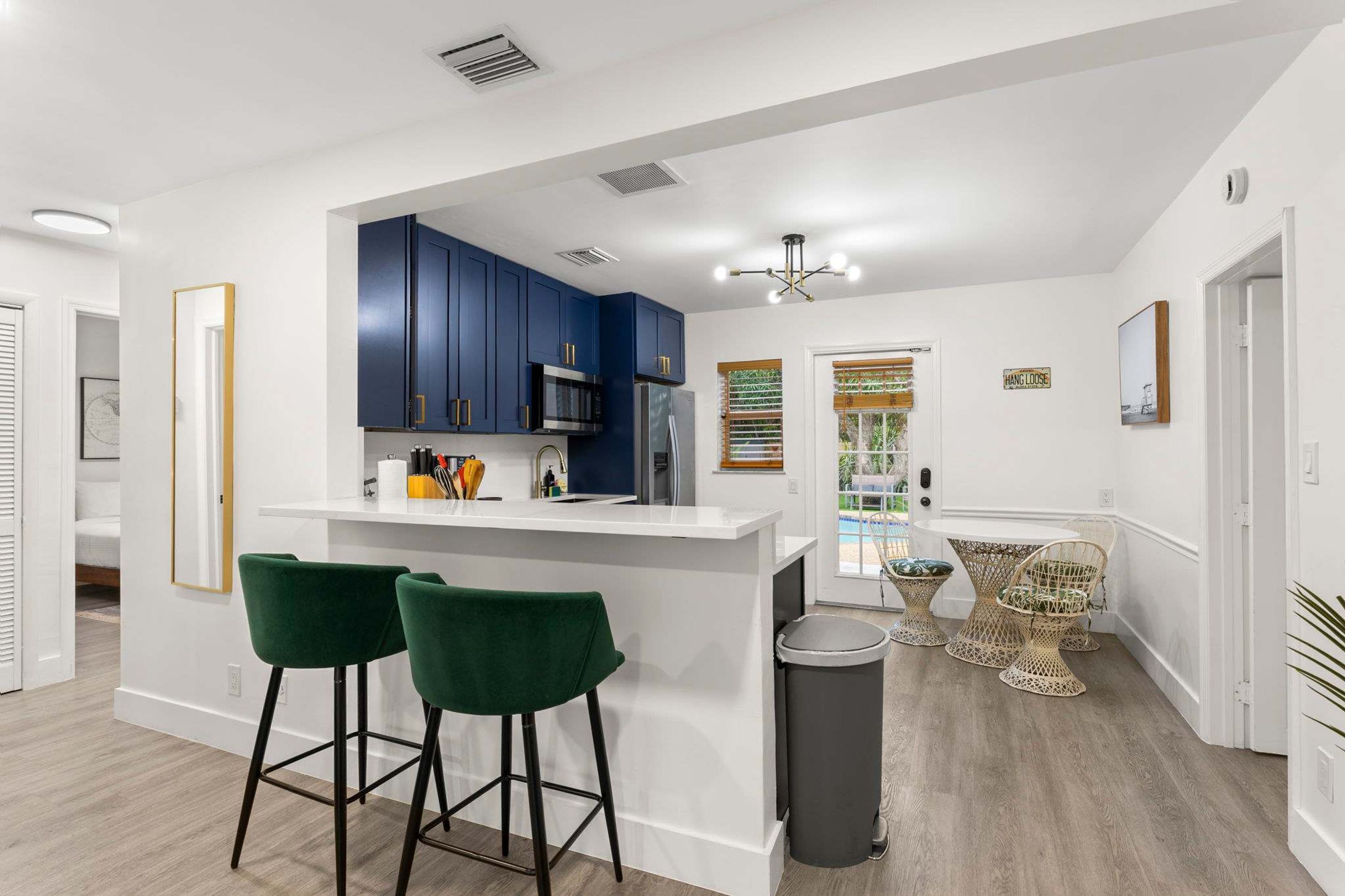 A modern kitchen with dark blue cabinets, a white countertop, and stainless steel appliances. There are two green bar stools and a small trash can.