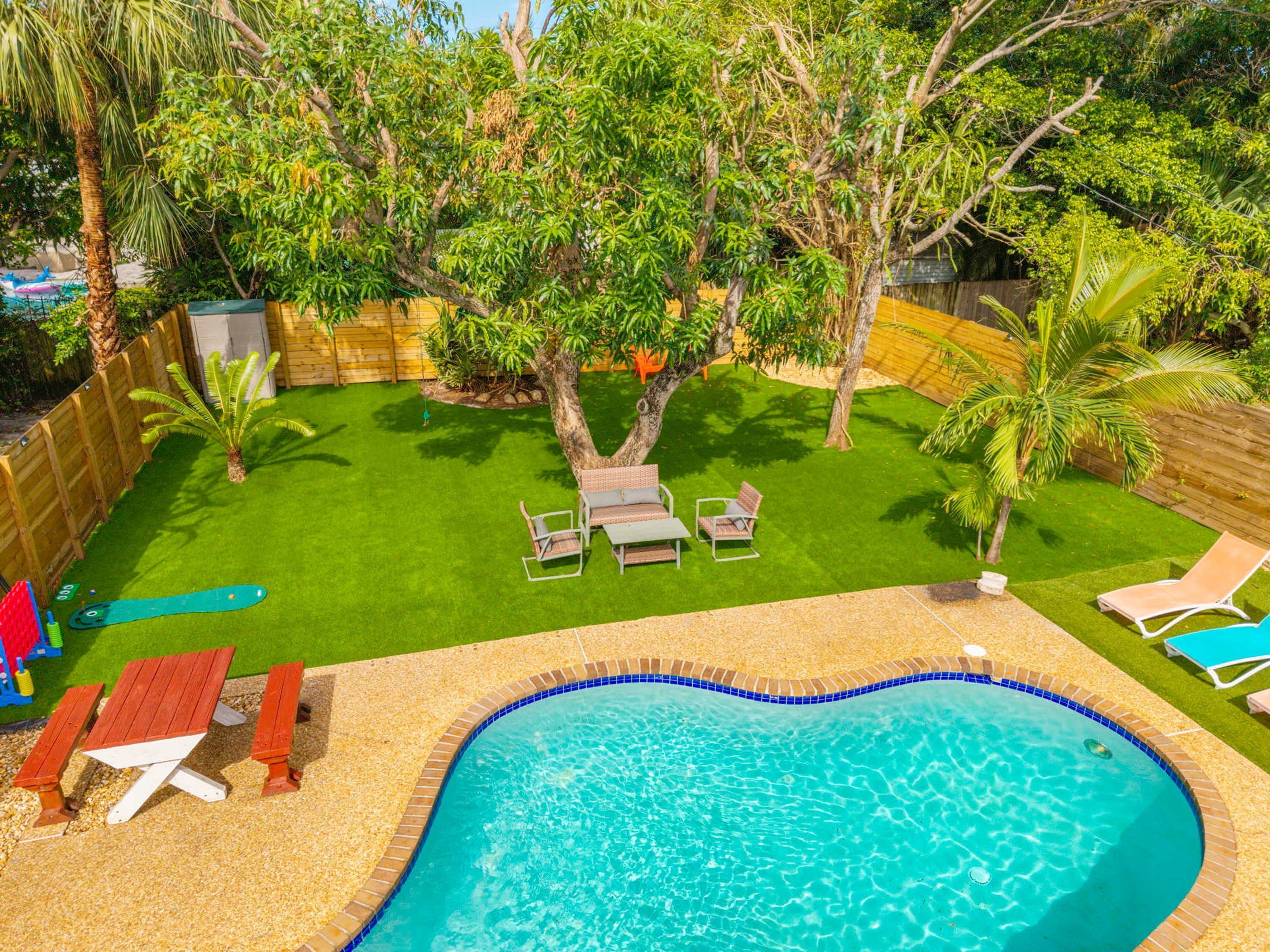 Un jardin avec une piscine, de l’herbe artificielle verte et une clôture en bois.