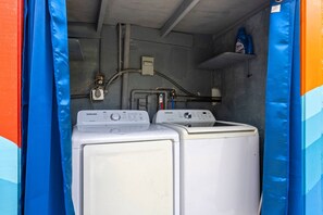 Ein Waschraum mit zwei weißen Waschmaschinen, einer blauen Waschmittelflasche und einem Warmwasserbereiter.