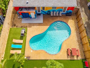 Ein Pool mit geschwungener Kante, umgeben von einem eingezäunten Garten mit Terrasse und Liegestühlen.