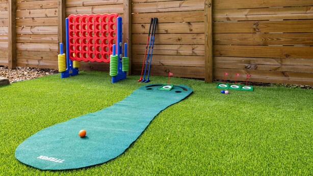 A children's play area with a green mat, a red climbing structure, and several poles. - Private Pool Patio Games BBQ Family Fun (Fort Lauderdale)