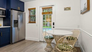 A modern kitchen with a stainless steel refrigerator, dark blue cabinets, and a white dining table with wicker chairs. - Private Pool Patio Games BBQ Family Fun (Fort Lauderdale)