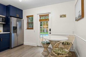 Eine moderne Küche mit einem Edelstahl-Kühlschrank, dunkelblauen Schränken und einem weißen Esstisch mit Korbstühlen.