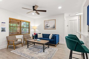 A modern living room with a blue sofa, two armchairs, a coffee table, a floor lamp, and a ceiling fan. - Private Pool Patio Games BBQ Family Fun (Fort Lauderdale)