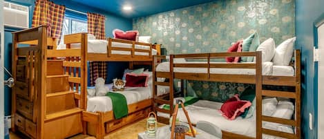 A bunk bed room with a table and chairs, a window with curtains, and a patterned wall.
