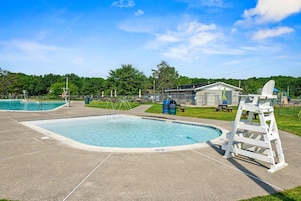 A swimming pool with a diving board, surrounded by a fenced area with picnic tables and a small building.