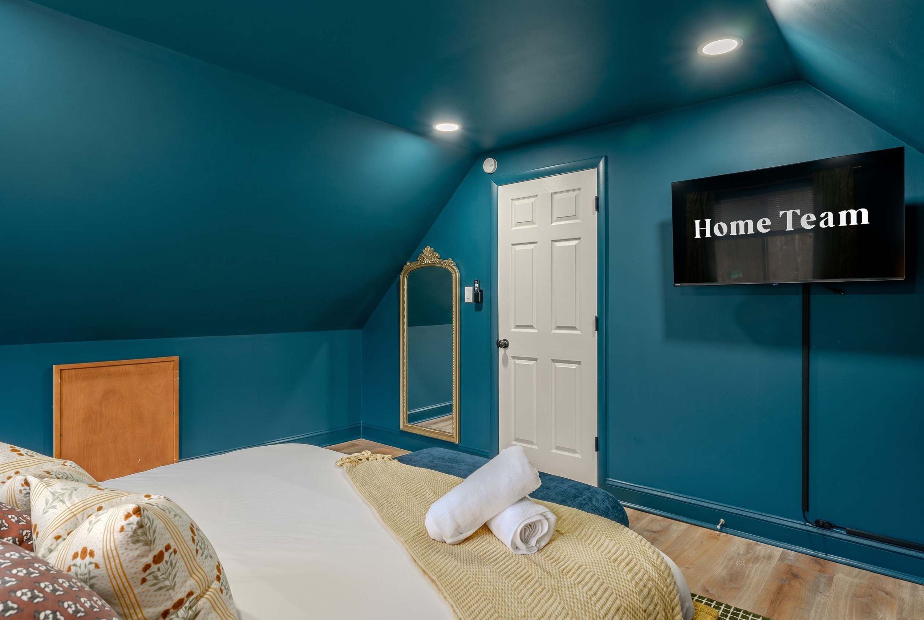 A bedroom with a bed, a TV, a door, and a mirror.