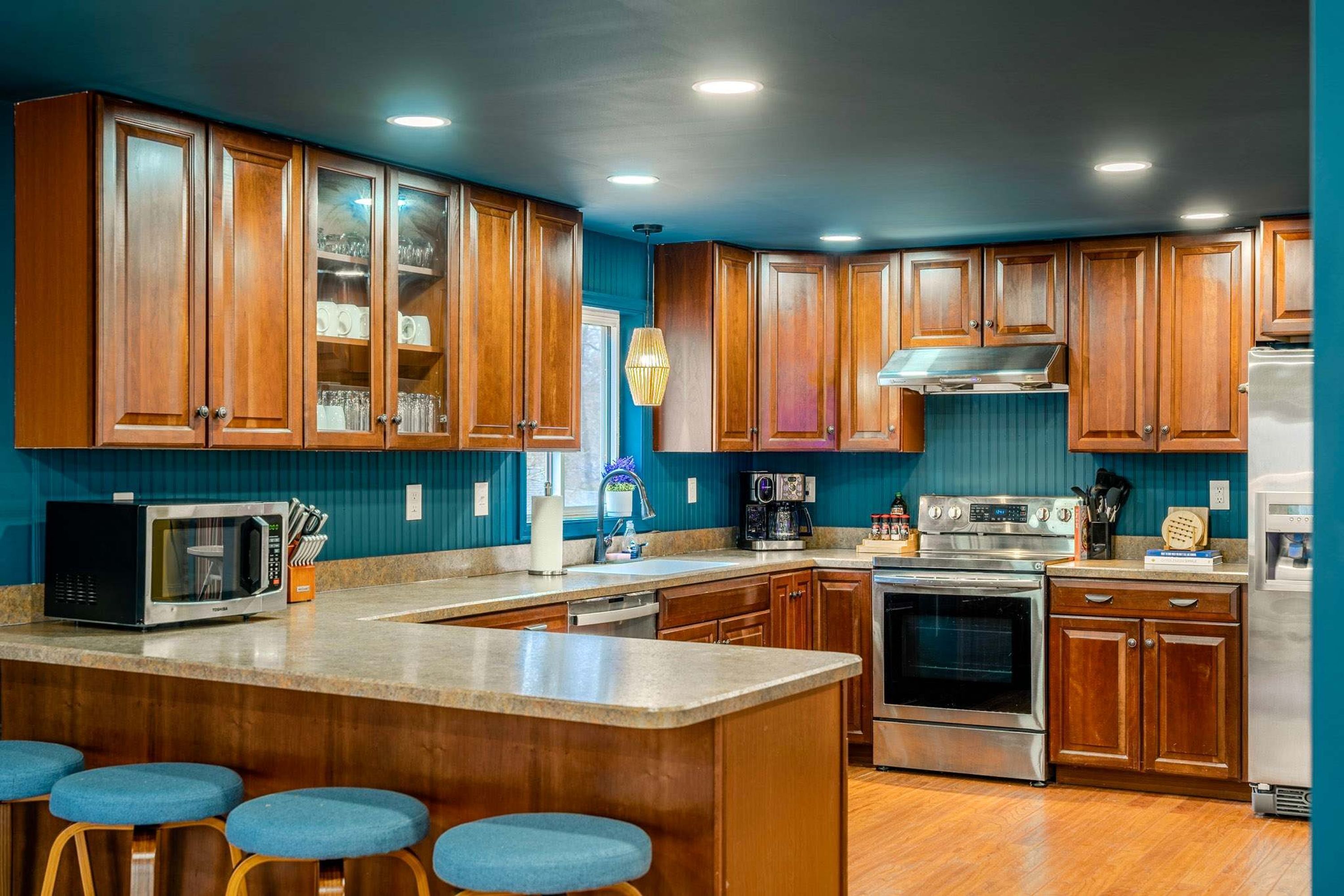 A kitchen with wooden cabinets, a central island with stools, a microwave, a coffee maker, and a stove.