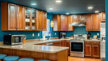 A kitchen with wooden cabinets, a central island with stools, a microwave, a coffee maker, and a stove.