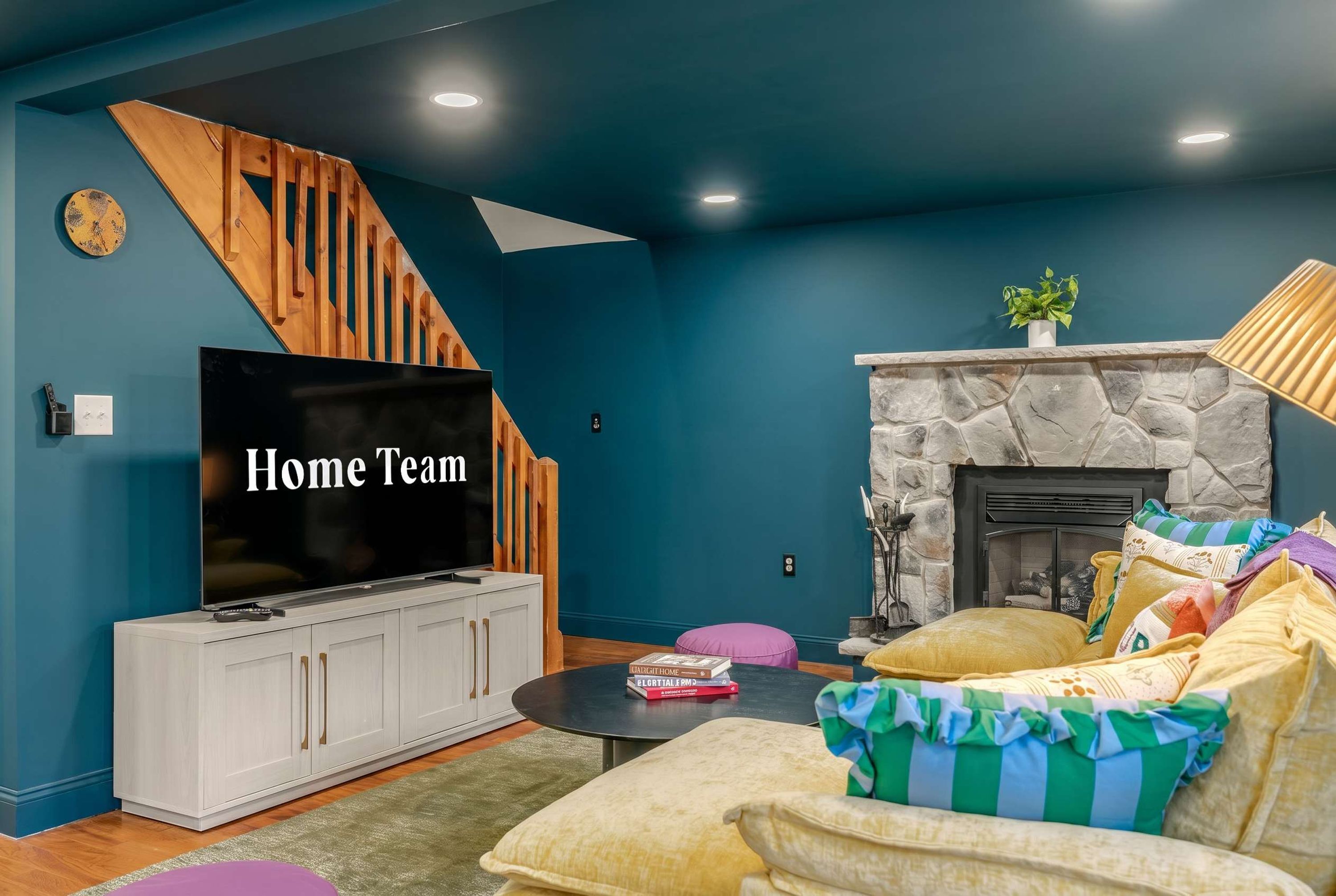 A living room with a TV, white cabinets, a stone fireplace, and a staircase.