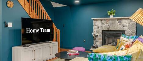 A living room with a TV, white cabinets, a stone fireplace, and a staircase.