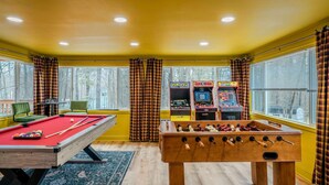 Una habitación con mesa de billar, mesa de futbolín y dos juegos de arcade.