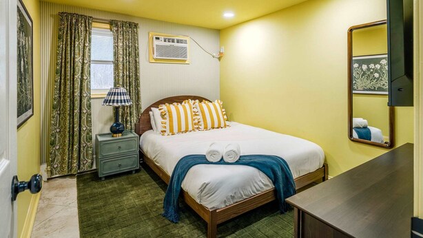 Una habitación de hotel con cama, mesita de noche, lámpara y espejo.