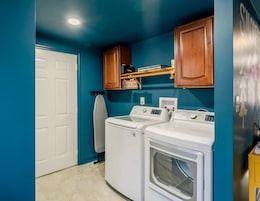 A laundry room with two front-loading washing machines, a dryer, and wooden cabinets above.